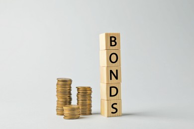 Word Bonds made of wooden cubes with letters and stacked coins on light grey background