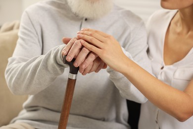 Photo of Senior man with walking cane and young woman indoors, closeup