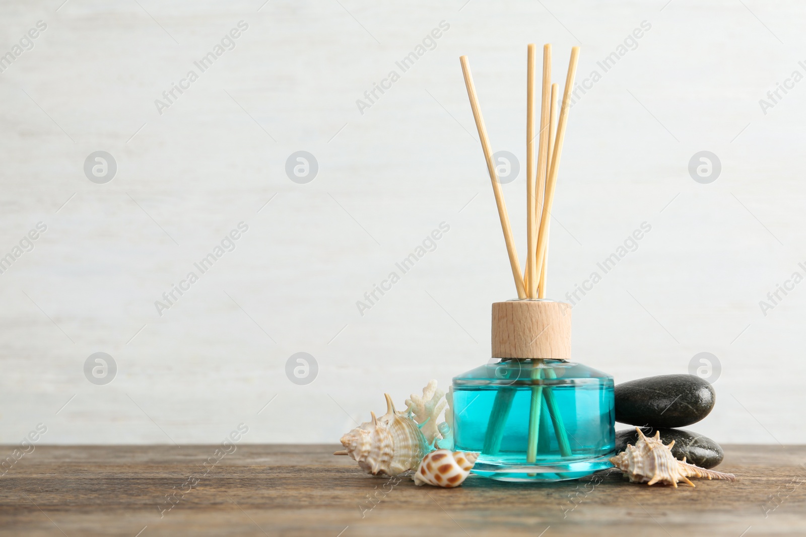Photo of Aromatic reed freshener, spa stones and sea shells on wooden table against light background. Space for text