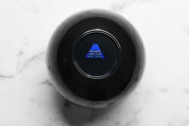 Photo of Magic eight ball with prediction Answer Unclear Ask Later on white marble table, top view
