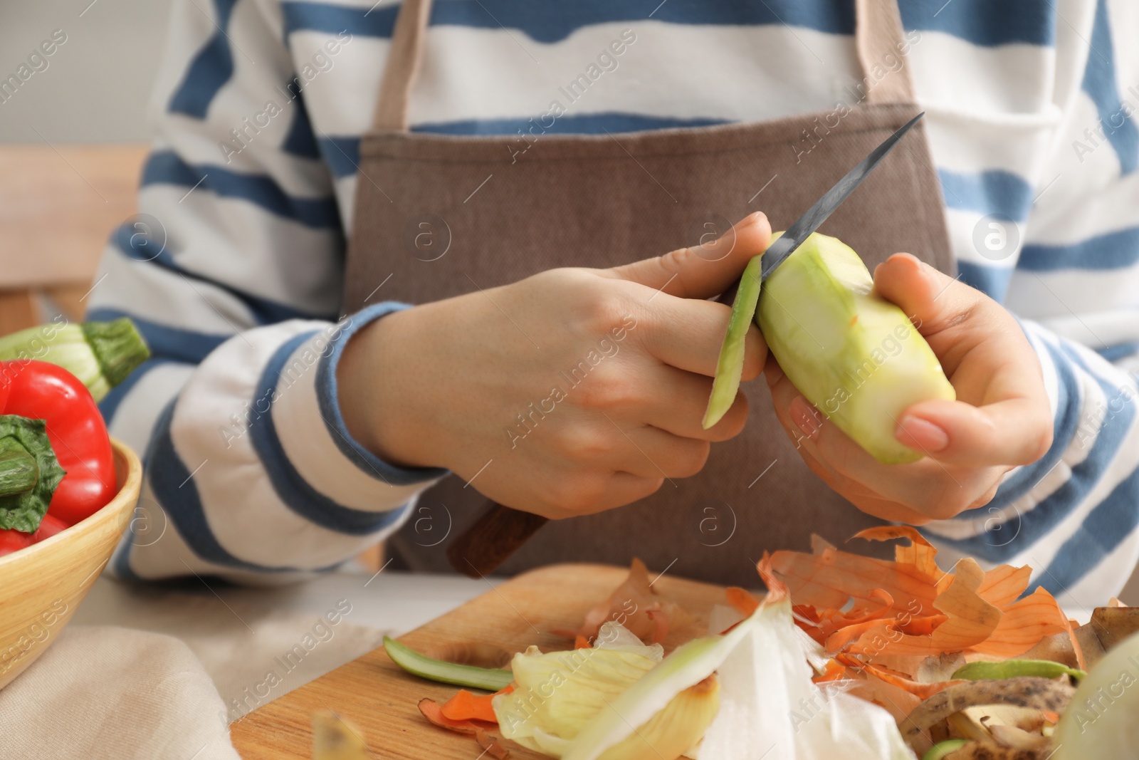 Photo of Woman peeling fresh zucchini with knife at table indoors, closeup