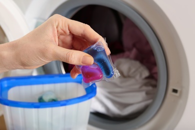 Photo of Woman holding laundry detergent capsule near washing machine, closeup