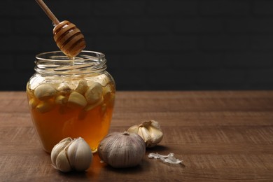 Photo of Natural honey dripping from dipper into glass jar with garlic on wooden table. Space for text