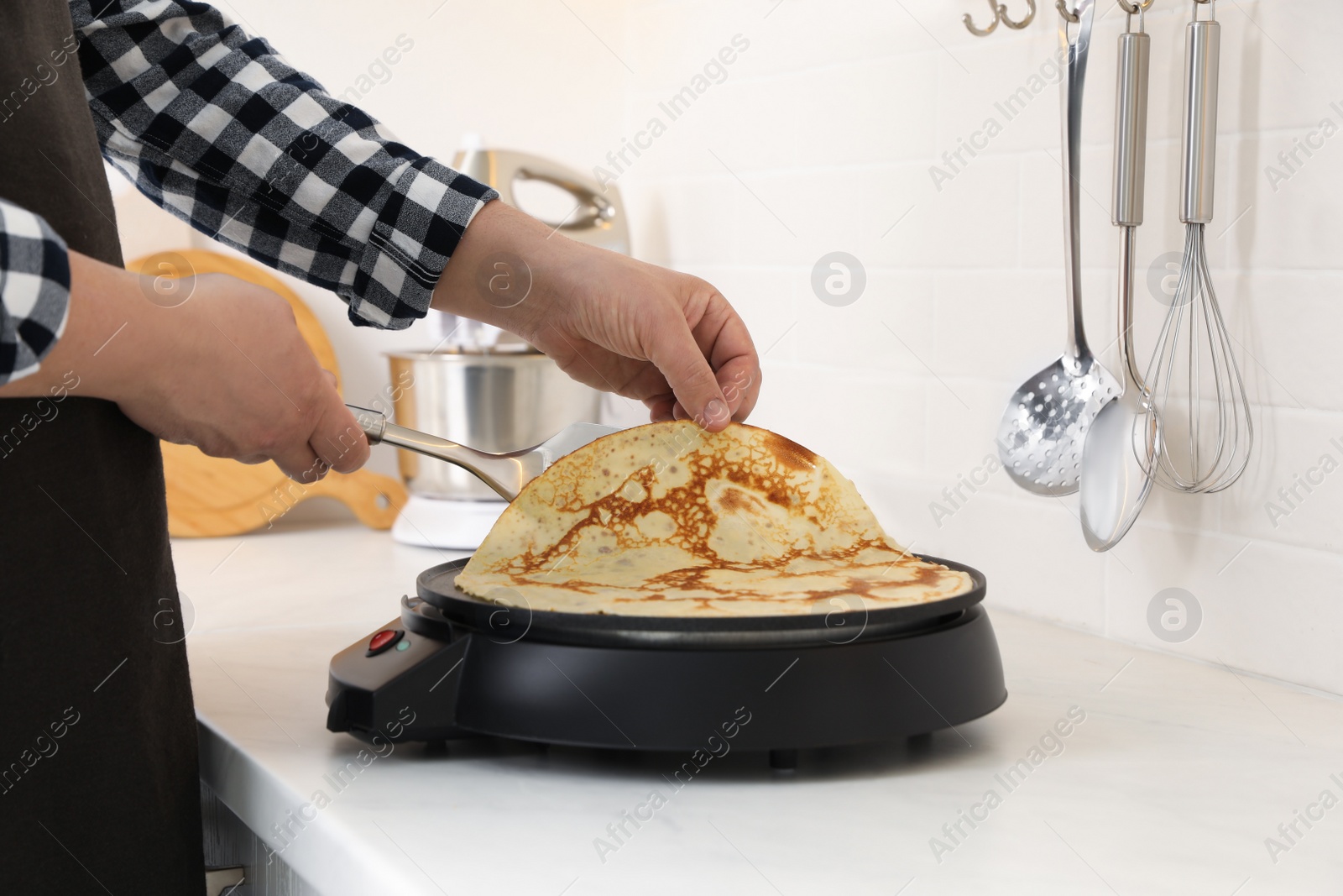 Photo of Man cooking delicious crepe on electric pancake maker in kitchen, closeup