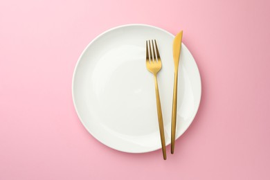 Plate, fork and knife on pink background, top view