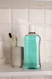 Photo of Bottle of mouthwash and toothbrushes on white shelf in bathroom