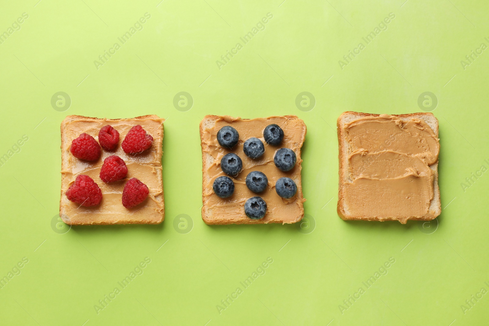 Photo of Tasty peanut butter sandwiches with fresh berries on light green background, flat lay