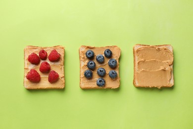 Photo of Tasty peanut butter sandwiches with fresh berries on light green background, flat lay