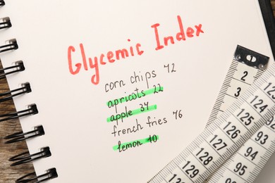 Glycemic Index. Notebook with information and measuring tape on table, top view