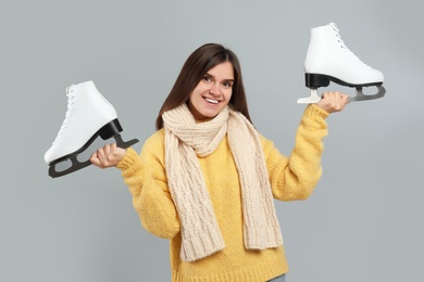 Happy woman with ice skates on grey background