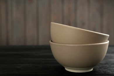 Photo of Stylish empty ceramic bowls on black wooden table, space for text. Cooking utensils