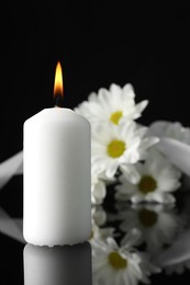 White chrysanthemum flowers and burning candle on black mirror surface in darkness, space for text. Funeral symbols