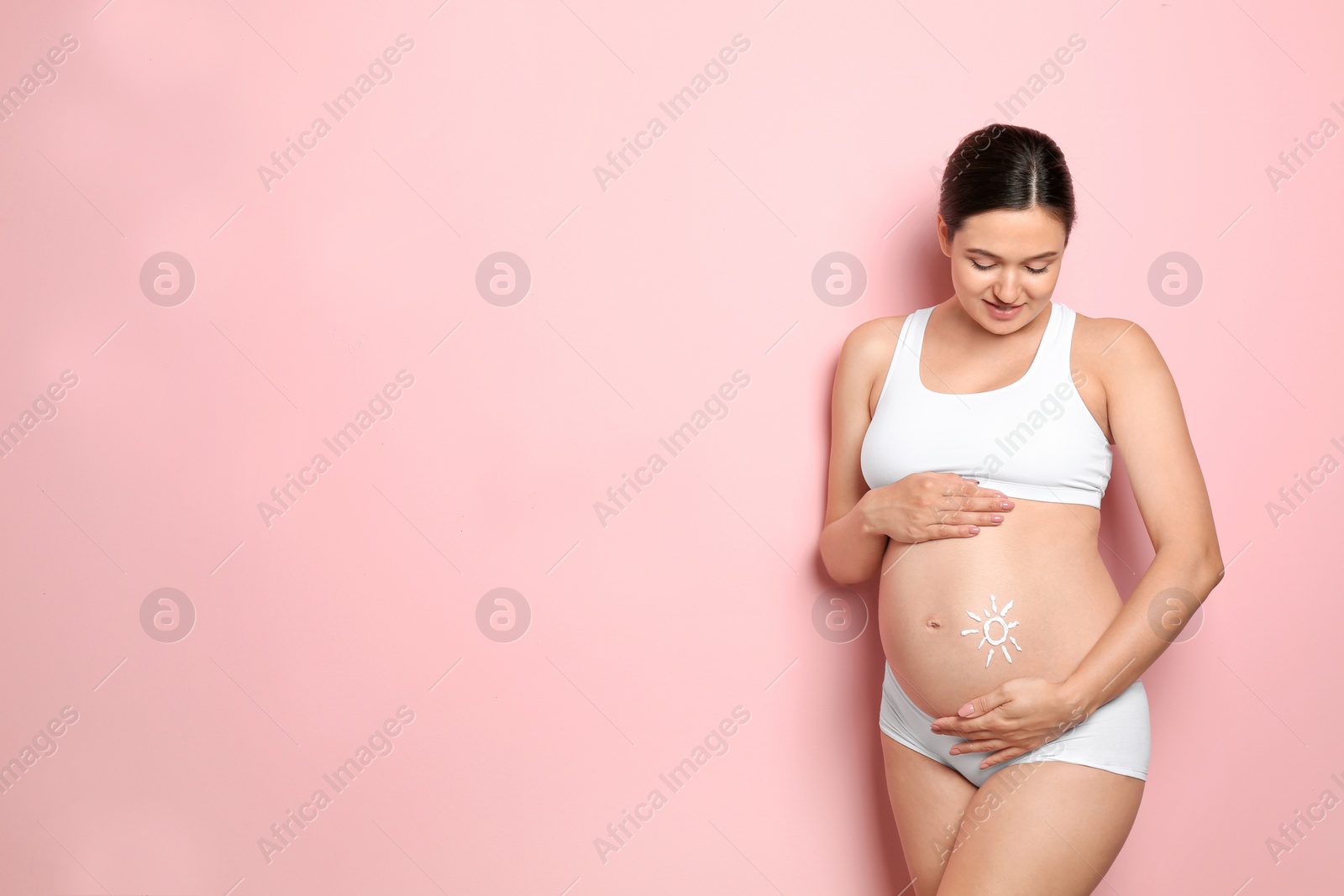 Photo of Sun painted with body cream on pregnant woman's belly against color background. Space for text