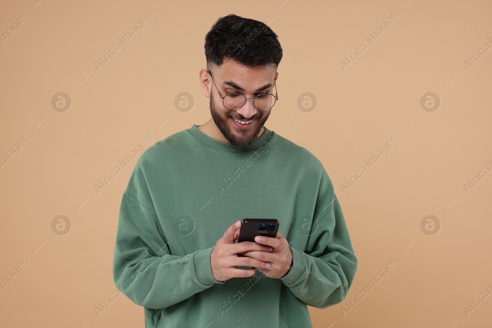 Photo of Happy young man using smartphone on beige background