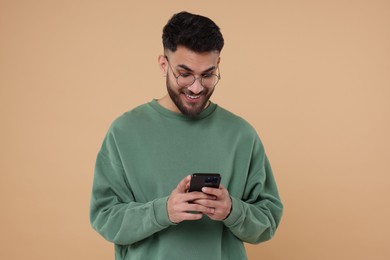 Happy young man using smartphone on beige background