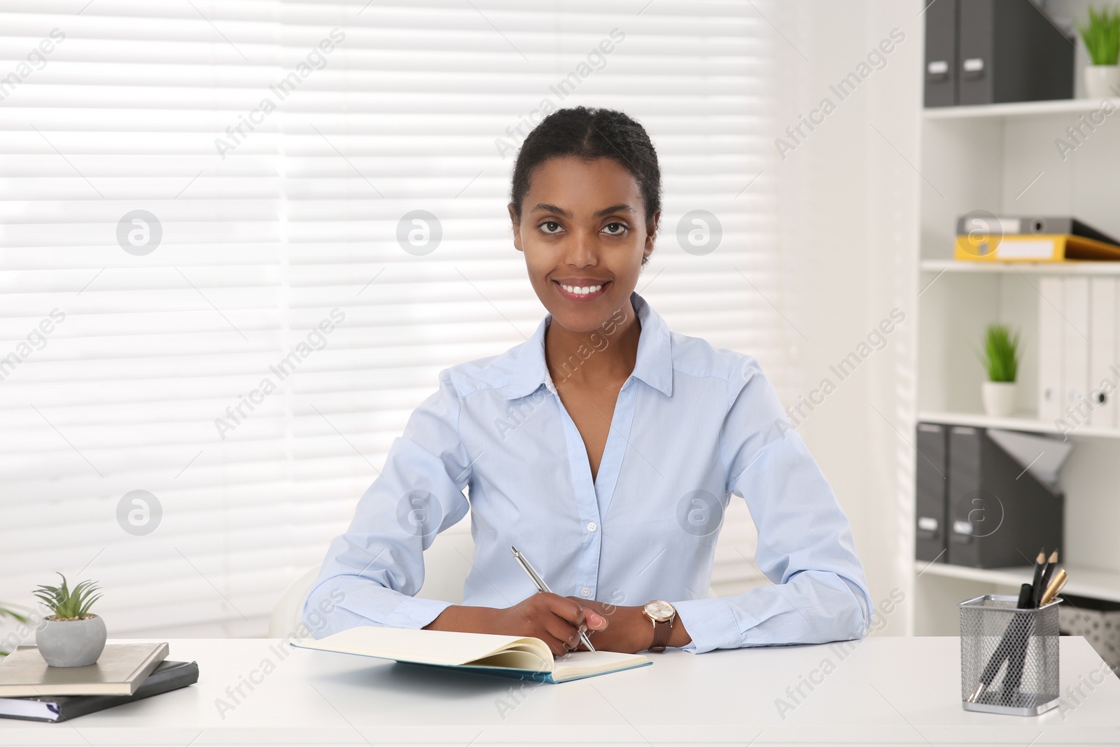 Photo of Smiling African American intern working at white table in office