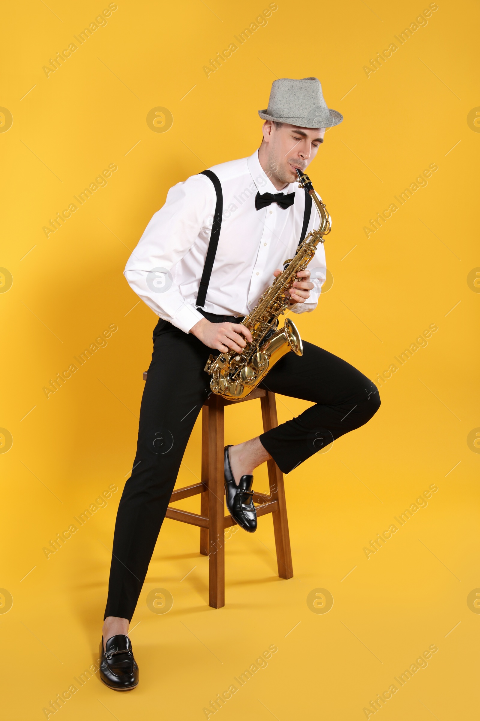 Photo of Young man in elegant outfit playing saxophone on yellow background