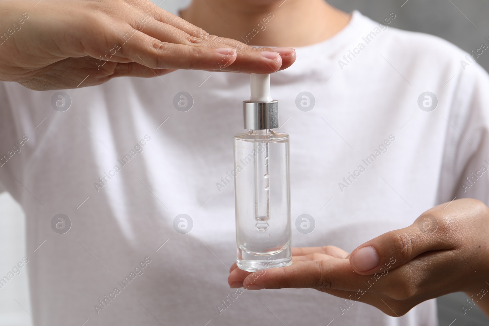 Photo of Woman with bottle of cosmetic serum on blurred background, closeup