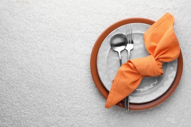 Photo of Stylish setting with cutlery, napkin and plates on light textured table, top view. Space for text