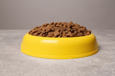 Photo of Dry food in yellow pet bowl on grey surface