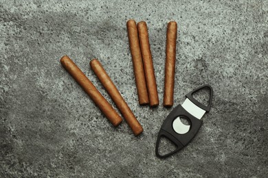 Photo of Many cigars and guillotine cutter on grey table, flat lay