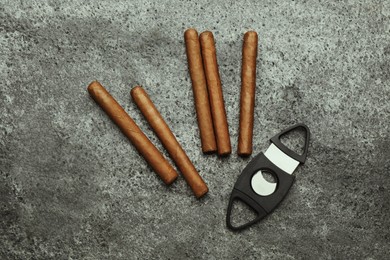 Many cigars and guillotine cutter on grey table, flat lay