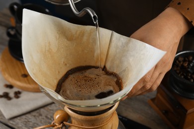 Photo of Woman pouring hot water into glass chemex coffeemaker with paper filter at table, closeup
