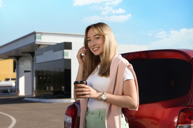 Beautiful young woman with coffee near car at gas station