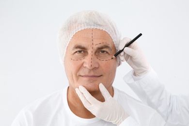 Photo of Doctor marking senior man face before cosmetic surgery on white background