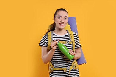Photo of Smiling young woman with backpack and thermo bottle on orange background. Active tourism