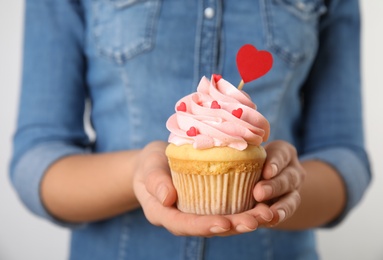 Photo of Woman holding tasty cupcake for Valentine's Day on light background, closeup