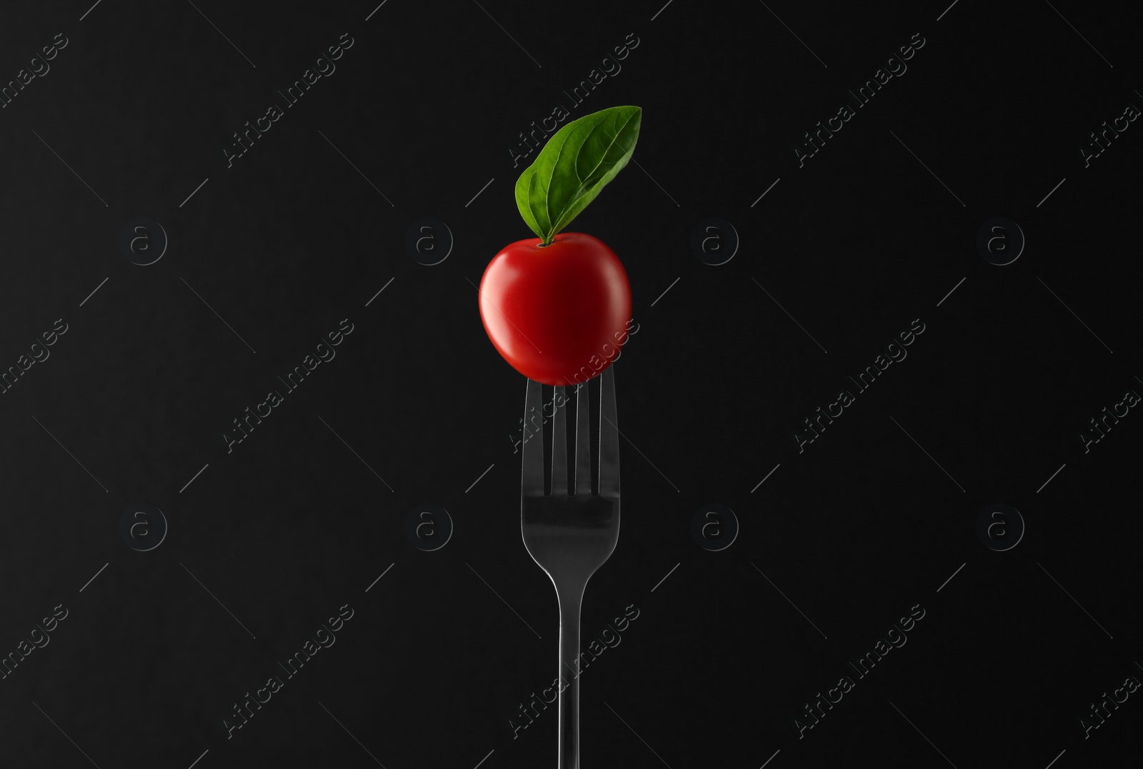 Photo of Fork with cherry tomato and basil on black background