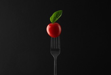 Photo of Fork with cherry tomato and basil on black background
