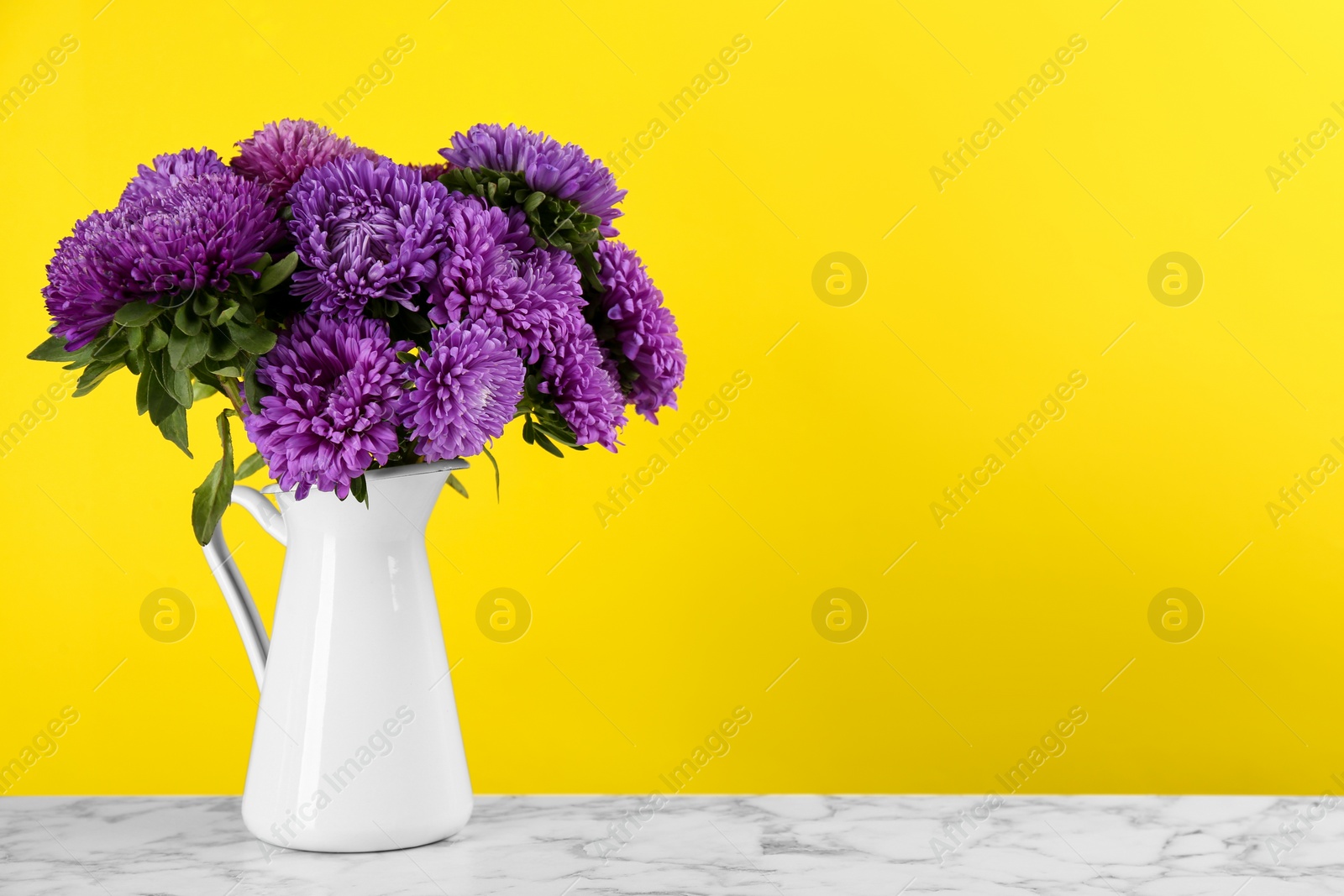 Photo of Beautiful asters in jug on table against yellow background, space for text. Autumn flowers