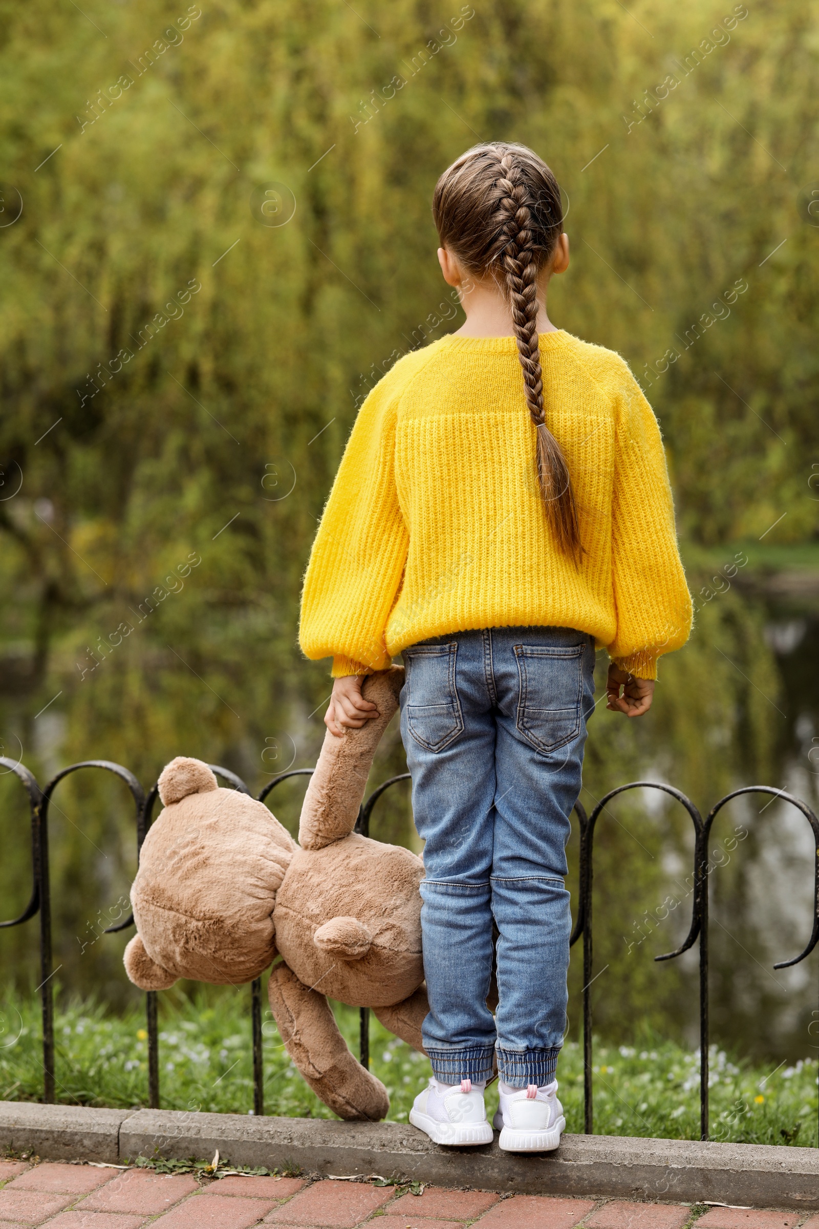 Photo of Little girl with teddy bear outdoors, back view