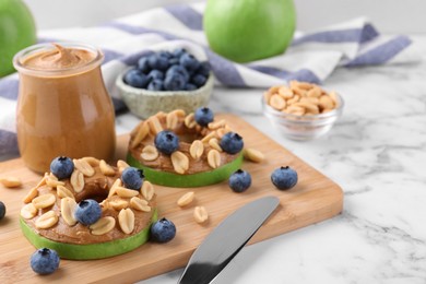 Slices of fresh apple with peanut butter, blueberries and nuts on white marble table