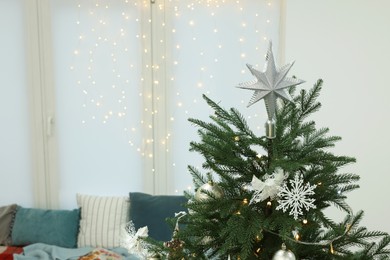 Photo of Interior design. Beautiful Christmas tree near cozy window sill and festive lights in room, space for text