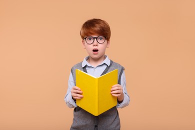 Photo of Surprised schoolboy with book on beige background
