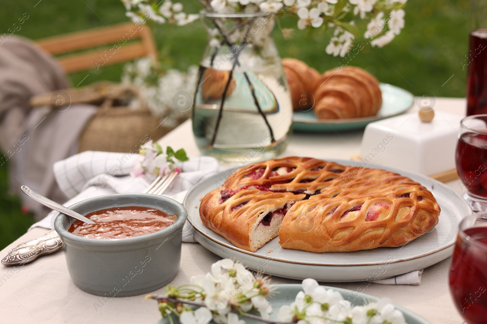 Photo of Stylish table setting with beautiful spring flowers, fruit drink and pie in garden