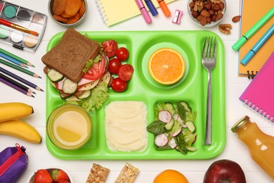 Photo of Serving tray of healthy food and stationery on white wooden table, flat lay. School lunch