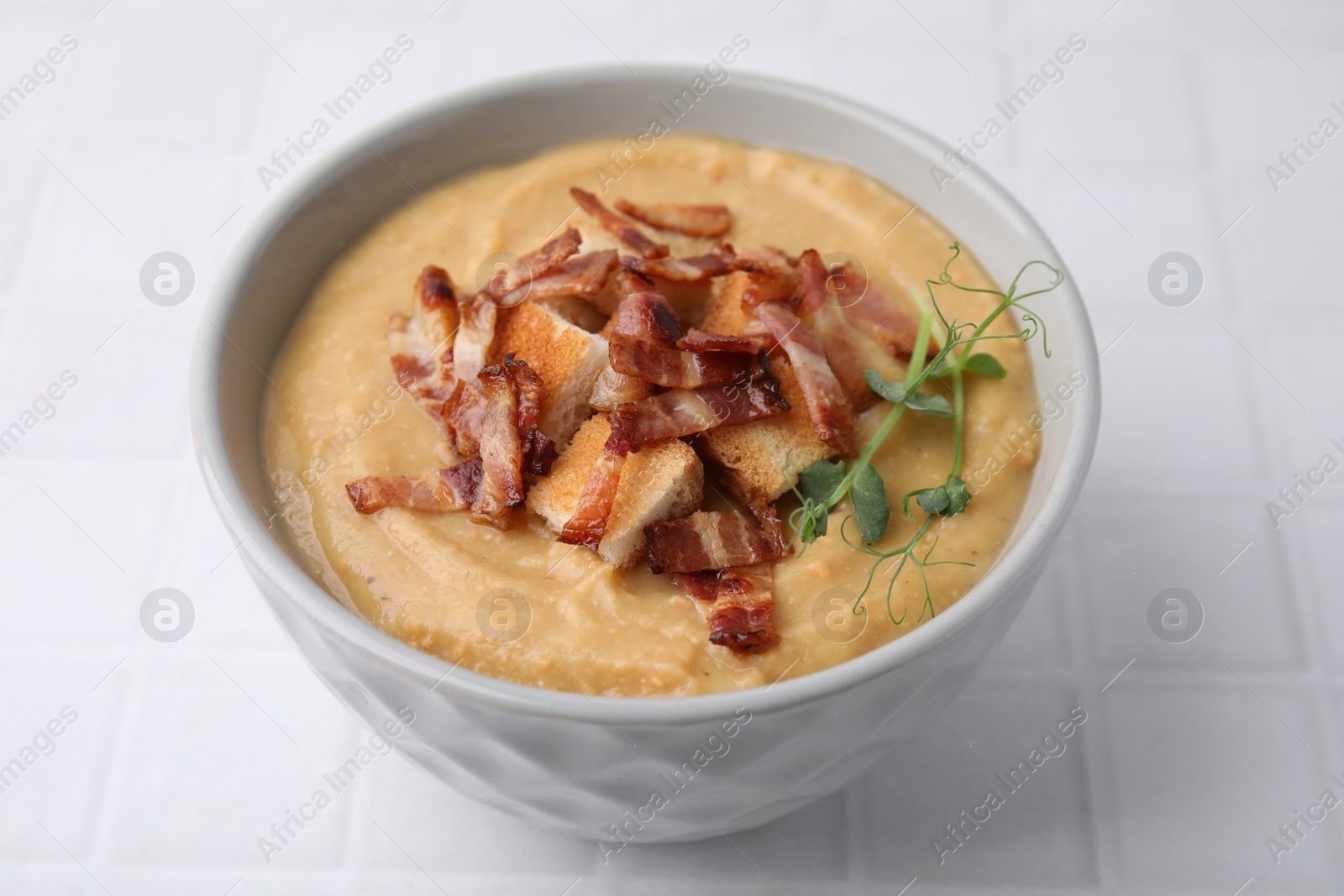 Photo of Delicious lentil soup with bacon and croutons on white tiled table, closeup