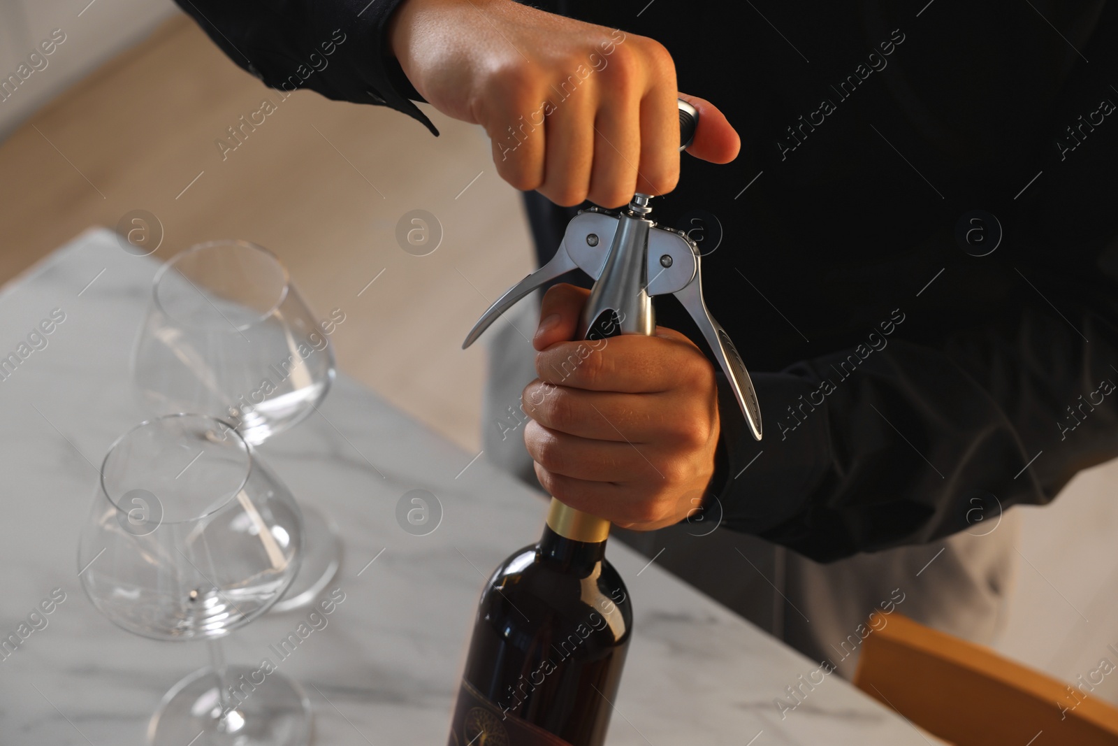 Photo of Man opening wine bottle with corkscrew at table indoors, closeup