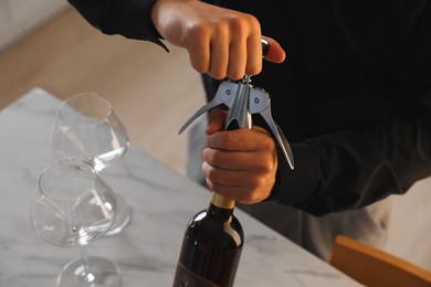 Photo of Man opening wine bottle with corkscrew at table indoors, closeup