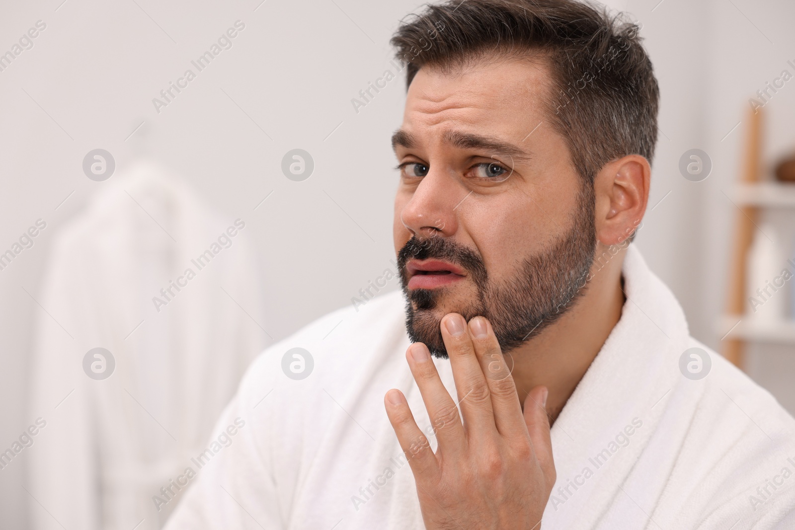 Photo of Skin problem. Confused man touching his face at home, space for text