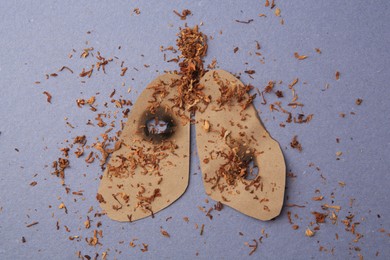 Photo of Paper cutout of human lungs with cigarette holes and tobacco on blue background, top view. No smoking concept