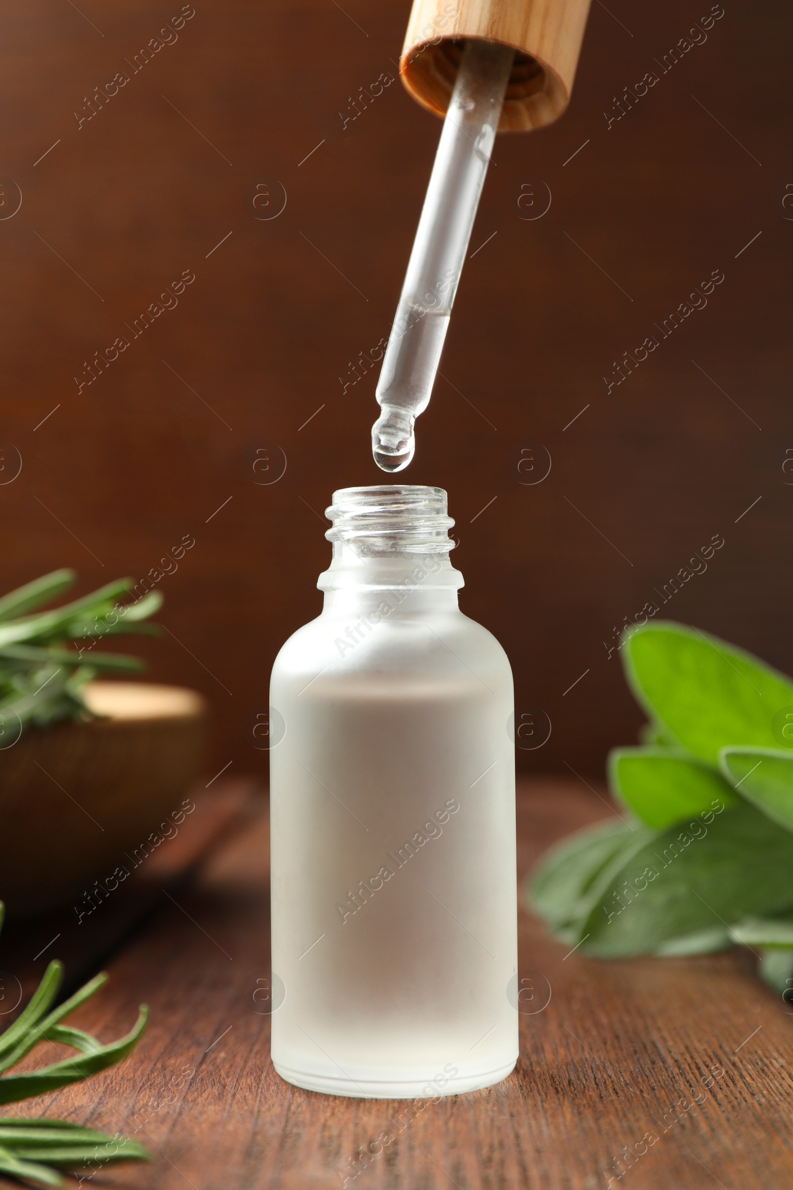 Photo of Dripping herbal essential oil from pipette into bottle on wooden table, closeup