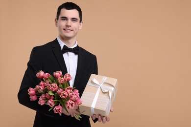 Photo of Happy young man with beautiful bouquet and present on beige background