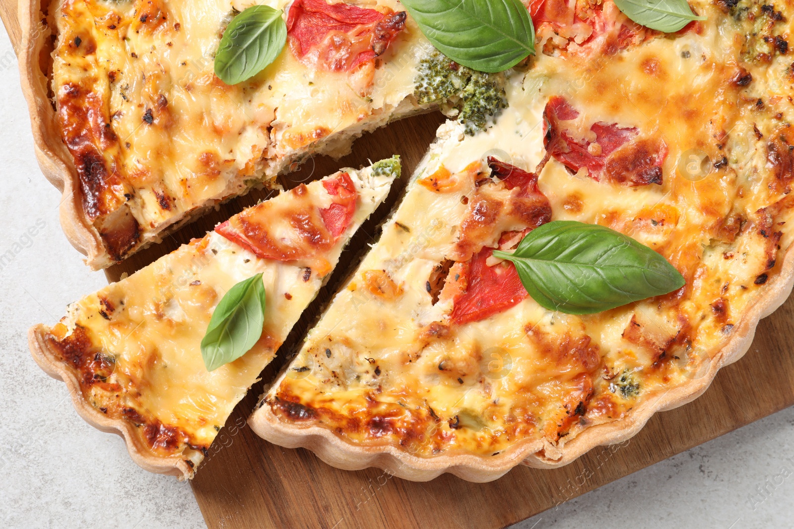 Photo of Tasty quiche with tomatoes, basil and cheese on light textured table, top view