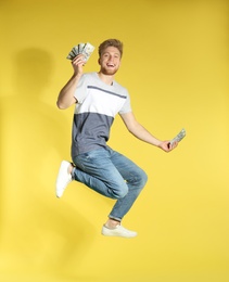 Young man jumping with money on color background