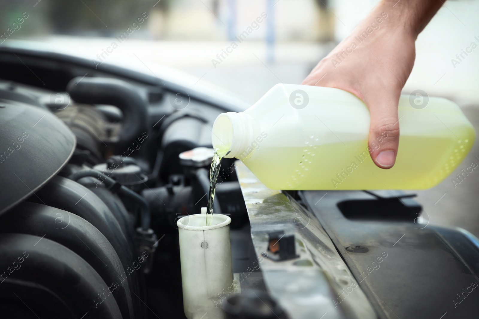 Photo of Man filling car radiator with antifreeze outdoors, closeup